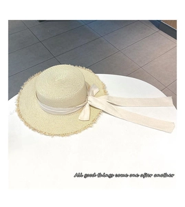Detail of straw sun hat featuring a white ribbon bow and rustic frayed edge brim