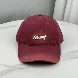 Close-up of heart embroidery on distressed burgundy baseball cap with frayed brim details