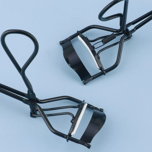 Premium black stainless steel eyelash curlers with white silicone pads on blue background