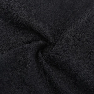 Dettaglio macro del tessuto in pizzo nero con ricami floreali e morbidi drappeggi chic