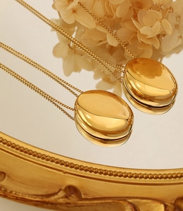 Collier avec pendentif ovale en or poli posé sur un plateau miroir rétro doré