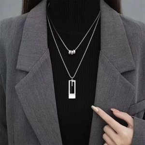 Close-up of a layered silver necklace with a rectangular hollow pendant on a black sweater