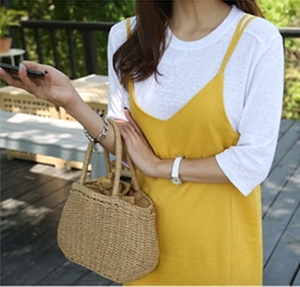 Detail of hand-woven straw tote bag paired with a yellow dress and a white wristwatch