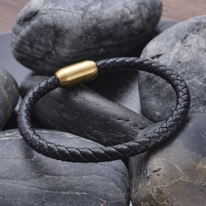 Braided black leather bracelet with a gold magnetic clasp displayed on dark grey pebbles