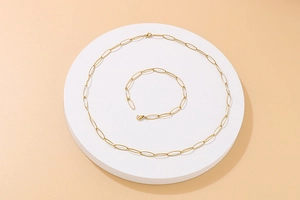 Detail view of golden oval link necklace and bracelet set on a white round display