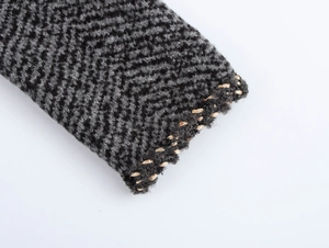 Macro shot of black herringbone knit fabric with elegant gold metallic thread edge
