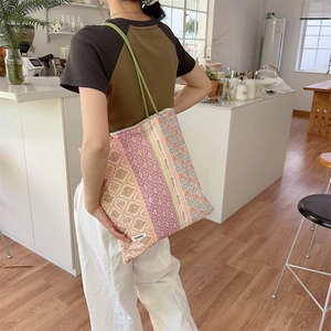 Détail du sac cabas en toile à fleurs avec bandoulière verte porté par un mannequin en décor