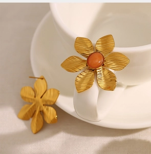 Detail of vintage gold flower earrings with orange gemstone and brushed texture finish