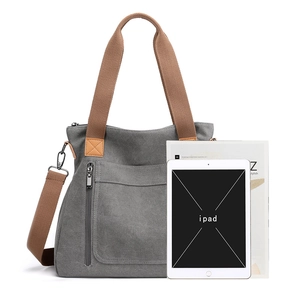 Grey canvas tote bag with brown straps and front pocket shown with a tablet for scale