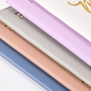 Detail of stacked PU leather passport holders in blue, pink, and grey with gold foil text