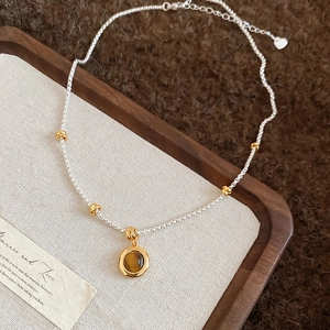 Detail of 18k gold plated tiger eye pendant with silver chain on rustic linen texture