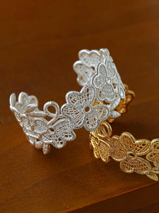 Close-up of vintage 18k gold and silver hollow flower open cuff bracelets on wood