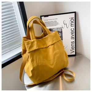 Detailed shot of yellow nylon tote bag with top handles on a metallic table