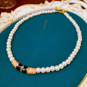 Detail of vintage necklace with pearls and enamel pendant on gold tray with green velvet