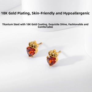 Close-up of heart-shaped crown earrings with red zircon in 18K gold plated steel