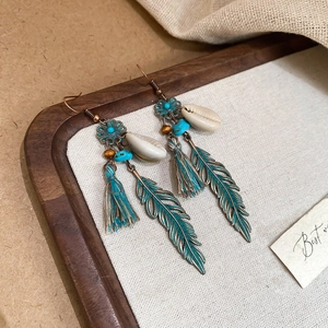 Detail of bohemian earrings with turquoise beads, shell, and teal feather on a wooden tray