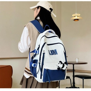 Blue and white canvas backpack with panda pendant and SJM lettering in a room