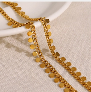 Macro detail of gold-plated disk charms on a delicate chain over linen fabric