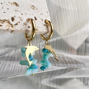 Detail of golden dolphin pendant earrings with light blue stones on stone display