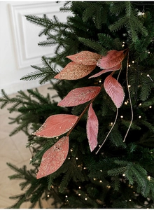 Close-up of glittery pink velvet leaf picks on a Christmas tree with warm lights