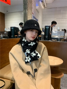 Close-up of knit scarf with black and white floral pattern and metal D-letter hat
