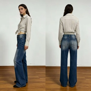 Detail of high-waist flared blue denim jeans with washed effect and fringed raw hem