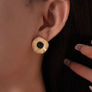 Gros plan de boucles d'oreilles rondes dorées vintage avec pierre carrée noire et texture