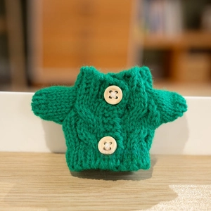 Detailed knit texture of a green mini doll cardigan with two cream buttons on wood