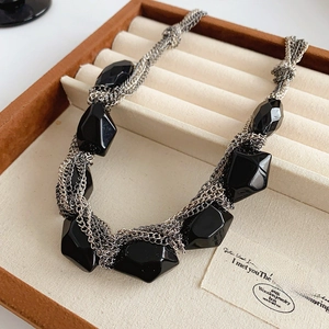 Detailed close-up of multilayered silver chain necklace with black geometric gemstone