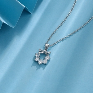 Silver bow necklace with zircon gemstone ring pendant on elegant blue paper background