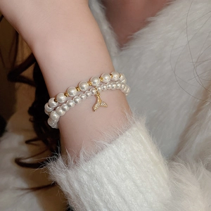 Close-up of double-layer pearl bracelet with a gold zircon fishtail charm on woman's wrist