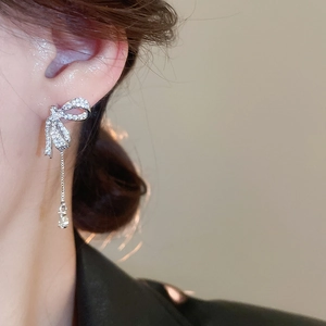 Detail view of silver bow earrings with long tassel fringes worn by a female model