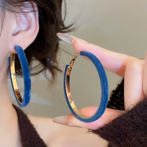 Close-up of large golden hoop earrings wrapped in soft blue velvet on a female model