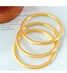 Three-piece set of solid gold matte metal bangles displayed on a soft aesthetic background