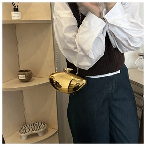 Close-up of golden bean-shaped metallic clutch bag with a sleek chain strap worn by a model