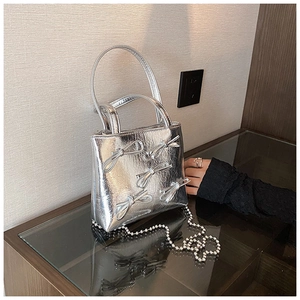 Detail of silver handbag with metallic bow embossing and beaded chain strap