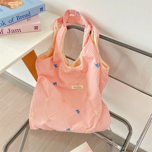 Detail of pink waffle texture tote bag with colorful embroidered bows and brand label
