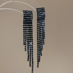 Gros plan d'élégantes boucles d'oreilles à longs pompons et strass sur fond beige