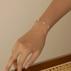 Detail of S925 silver cross bracelet with cubic zirconia and pearls on female wrist