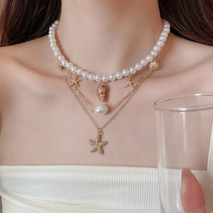 Detail of layered starfish and shell charms with baroque pearls on a gold necklace