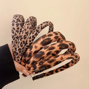 Hand holding stylish leopard print padded headbands in various brown and beige tones