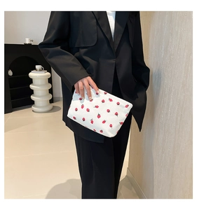 Close-up of white corduroy tote bag featuring red strawberry patterns on a model