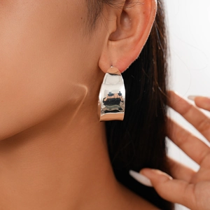 Close-up of a silver wide C-shape geometric hoop earring worn by a female model