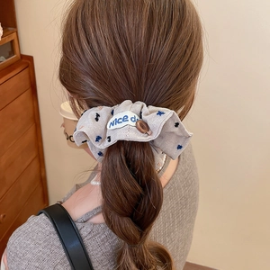 Detail of oversized ruffled floral scrunchie with decorative button and woven label