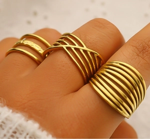 Detailed view of three 18K gold plated geometric rings worn on a hand in soft warm light