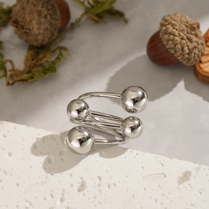 Makroaufnahme eines silbernen geometrischen Spiralrings mit vier polierten Perlen auf Stein