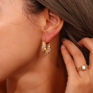 Dettaglio di orecchini a cerchio dorati con perle e anello intrecciato indossati da modella