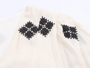 Detailed macro view of geometric embroidery and linen texture on a boho V-neck dress
