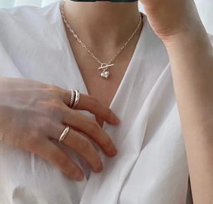 Detail of 925 sterling silver layered twist ring and heart pendant necklace on model