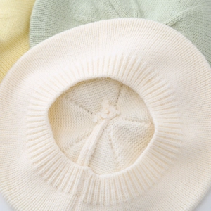 Creamy white knitted baby beret hat made of soft wool fabric shown in a detailed close-up view